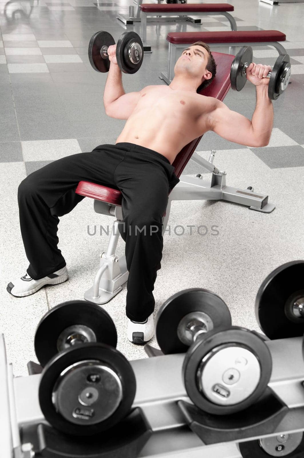 Man lying on a weight bench and exercising with dumbbells