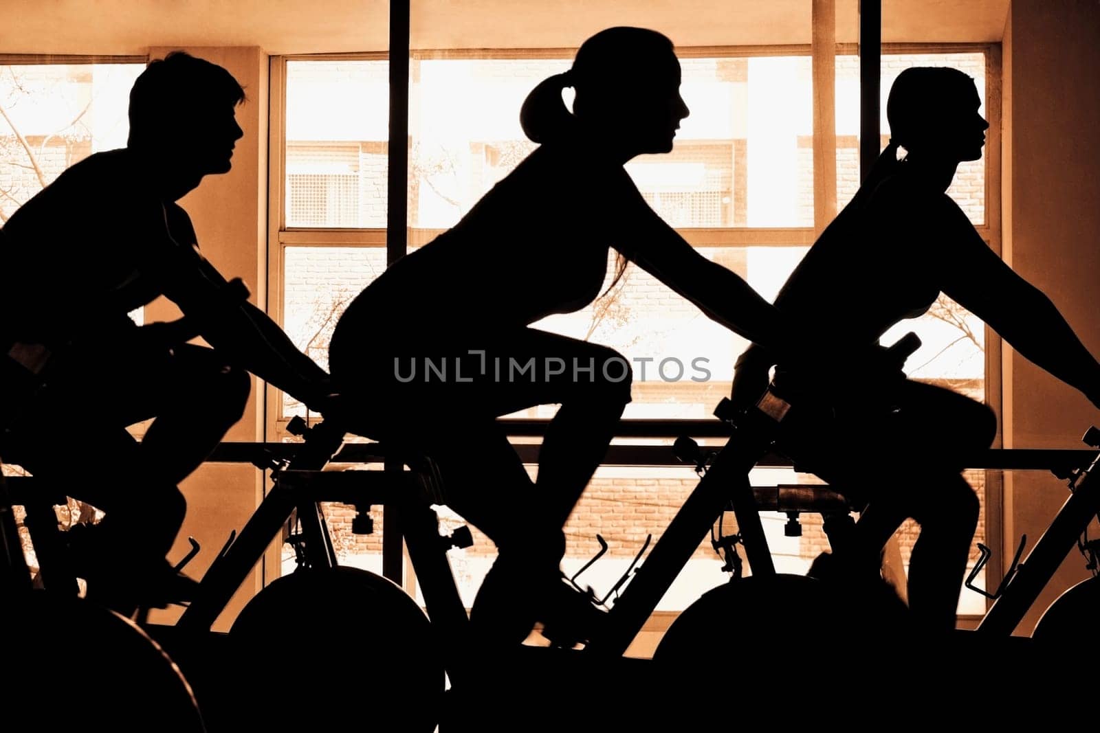 Silhouette of three people working out on exercise bikes in a gym