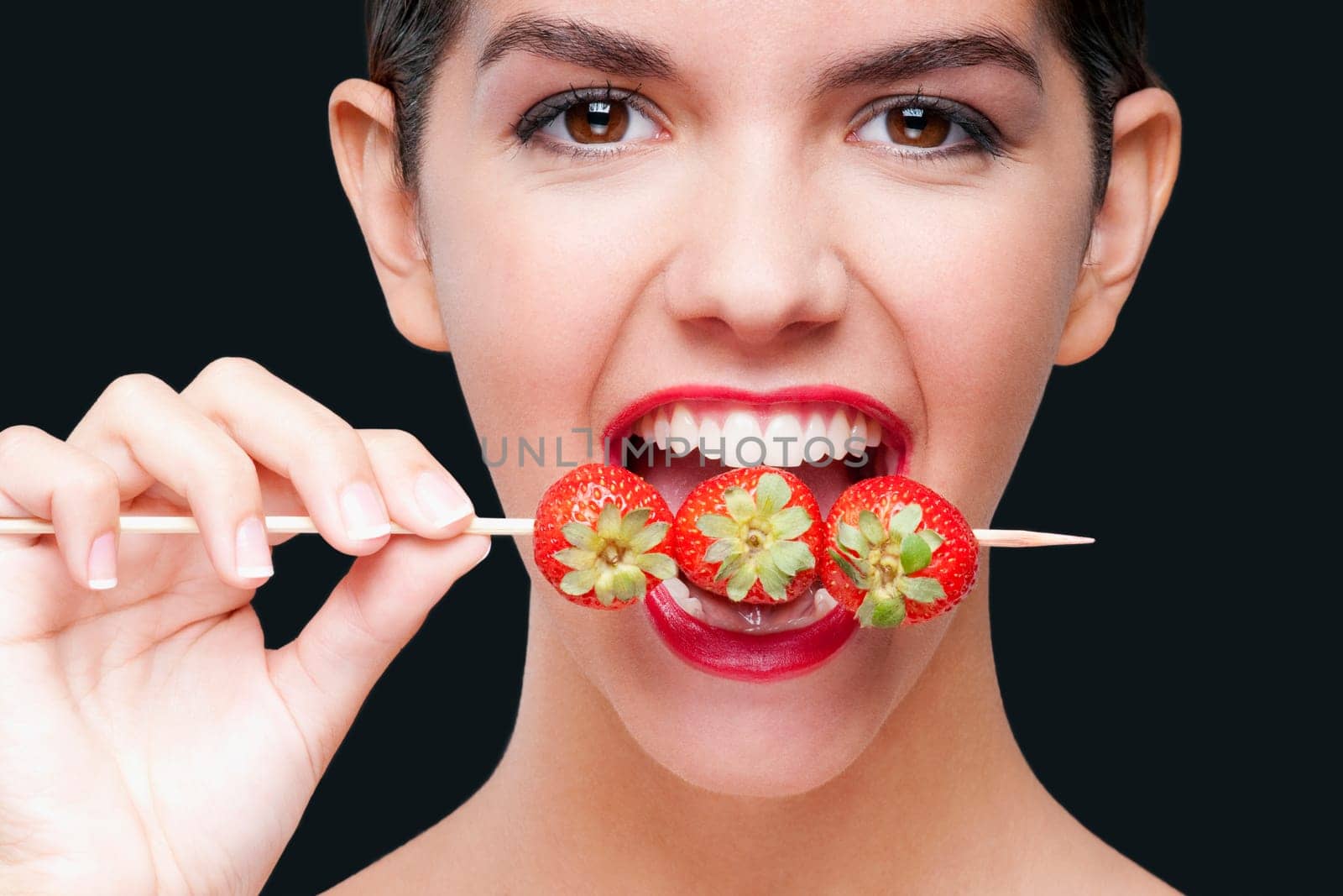 Close_up of a woman biting strawberries on a skewer