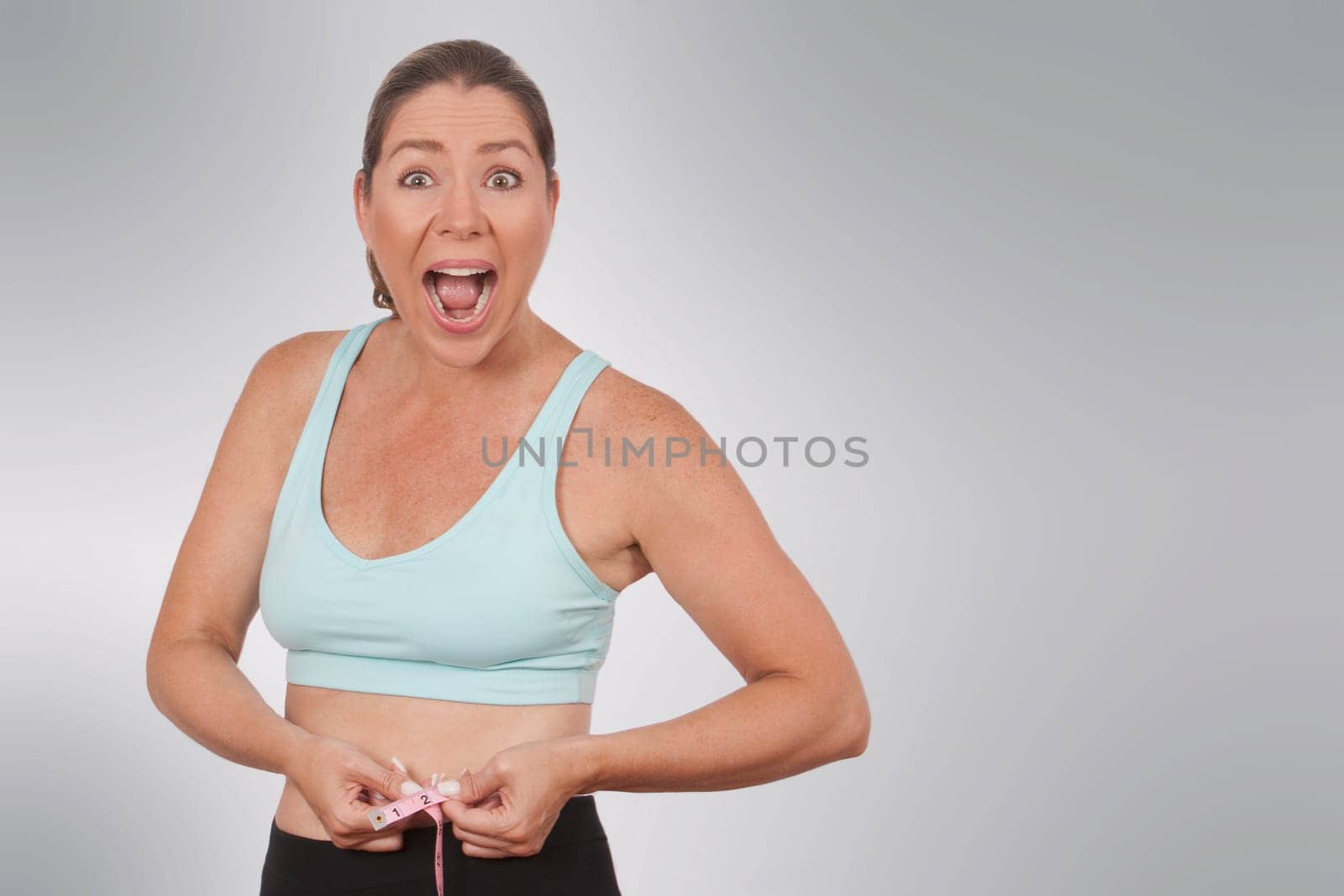 Woman looking surprised while measuring her waist with a tape measure
