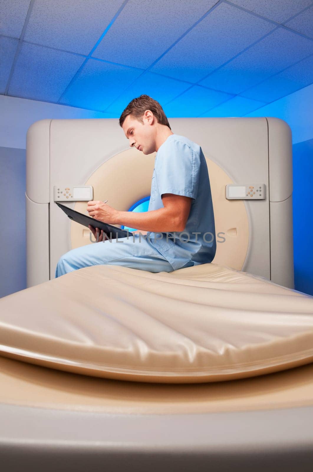Healthcare worker sitting on a CAT scan machine and writing on a clipboard