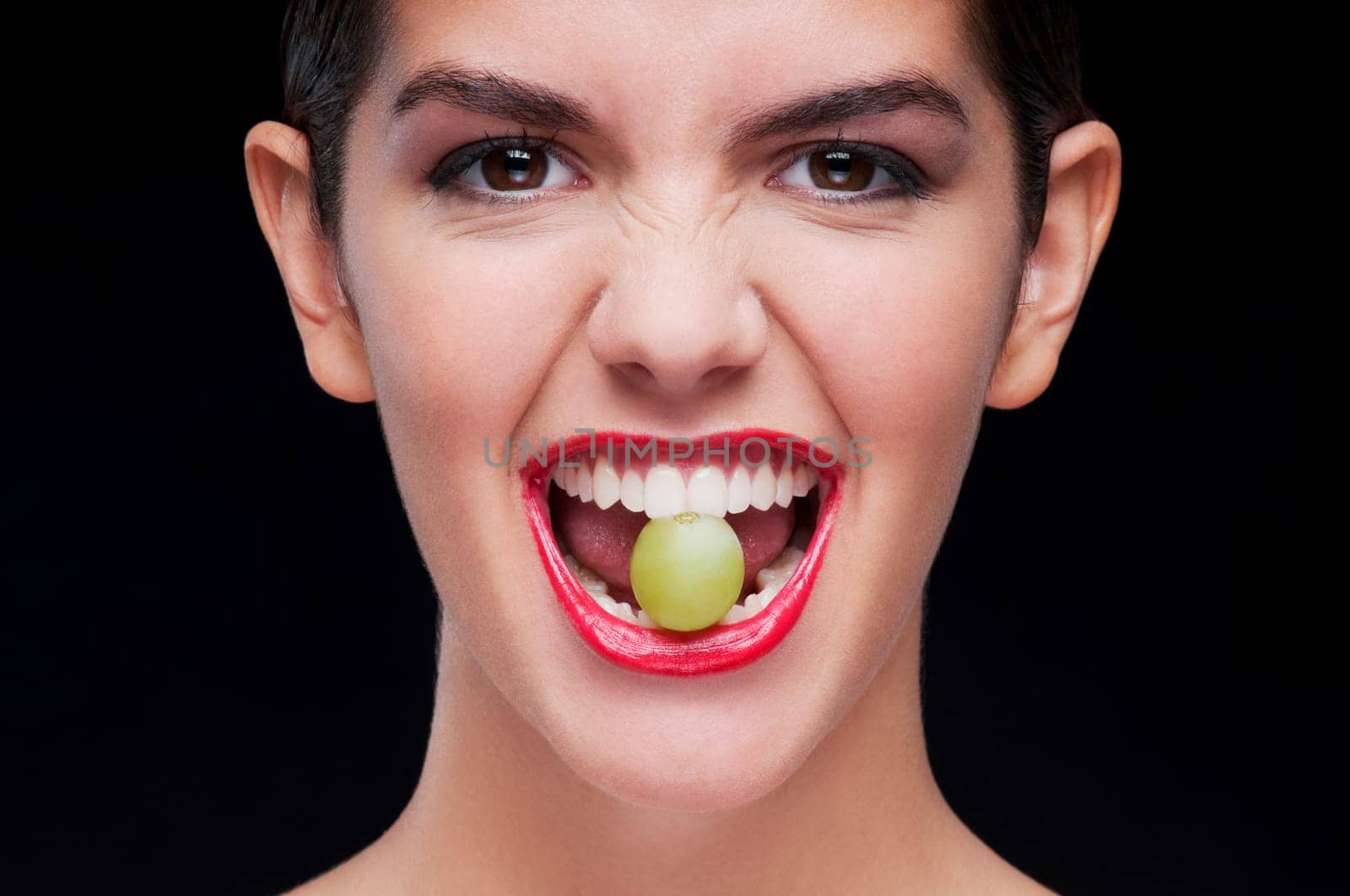 Woman holding a green grape between her teeth