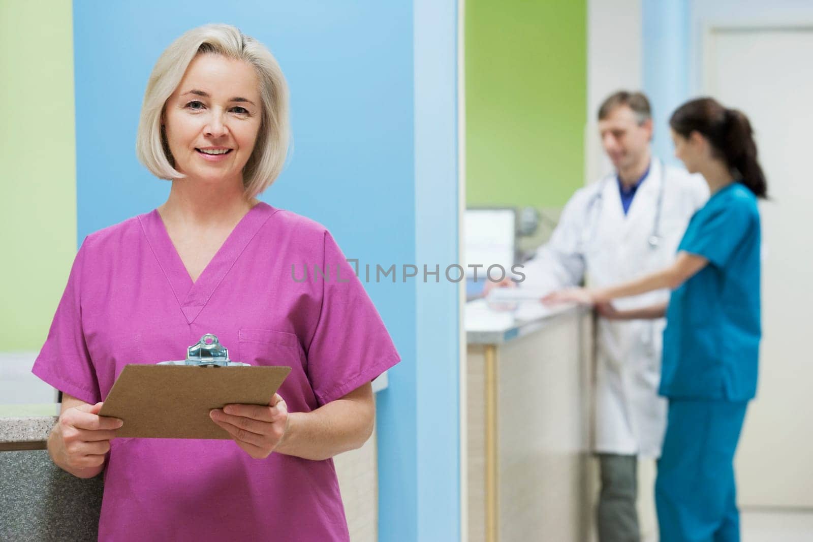 Female nurse holding a clipboard with a doctor and a nurse in the background