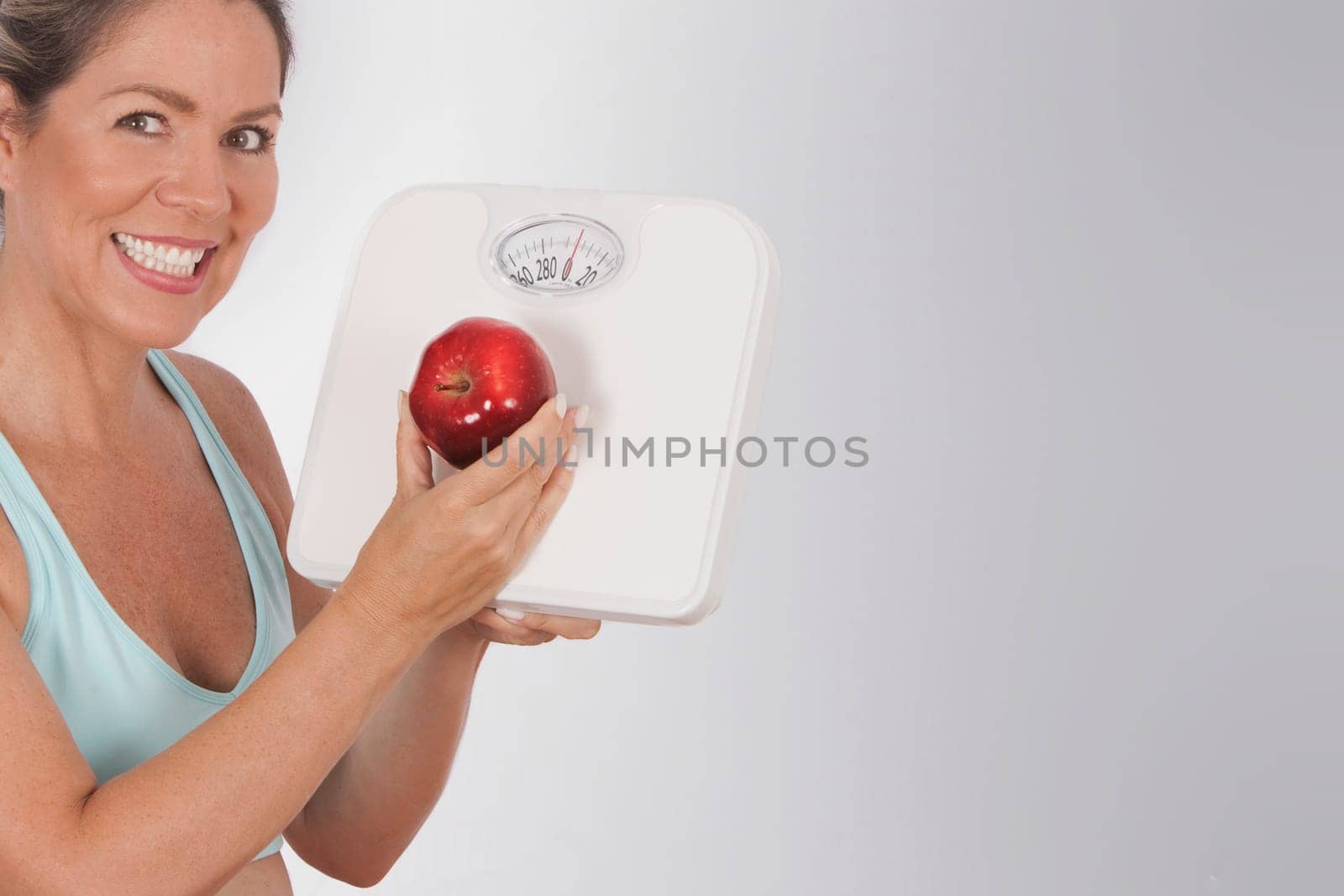Woman holding a bathroom scale and an apple and smiling