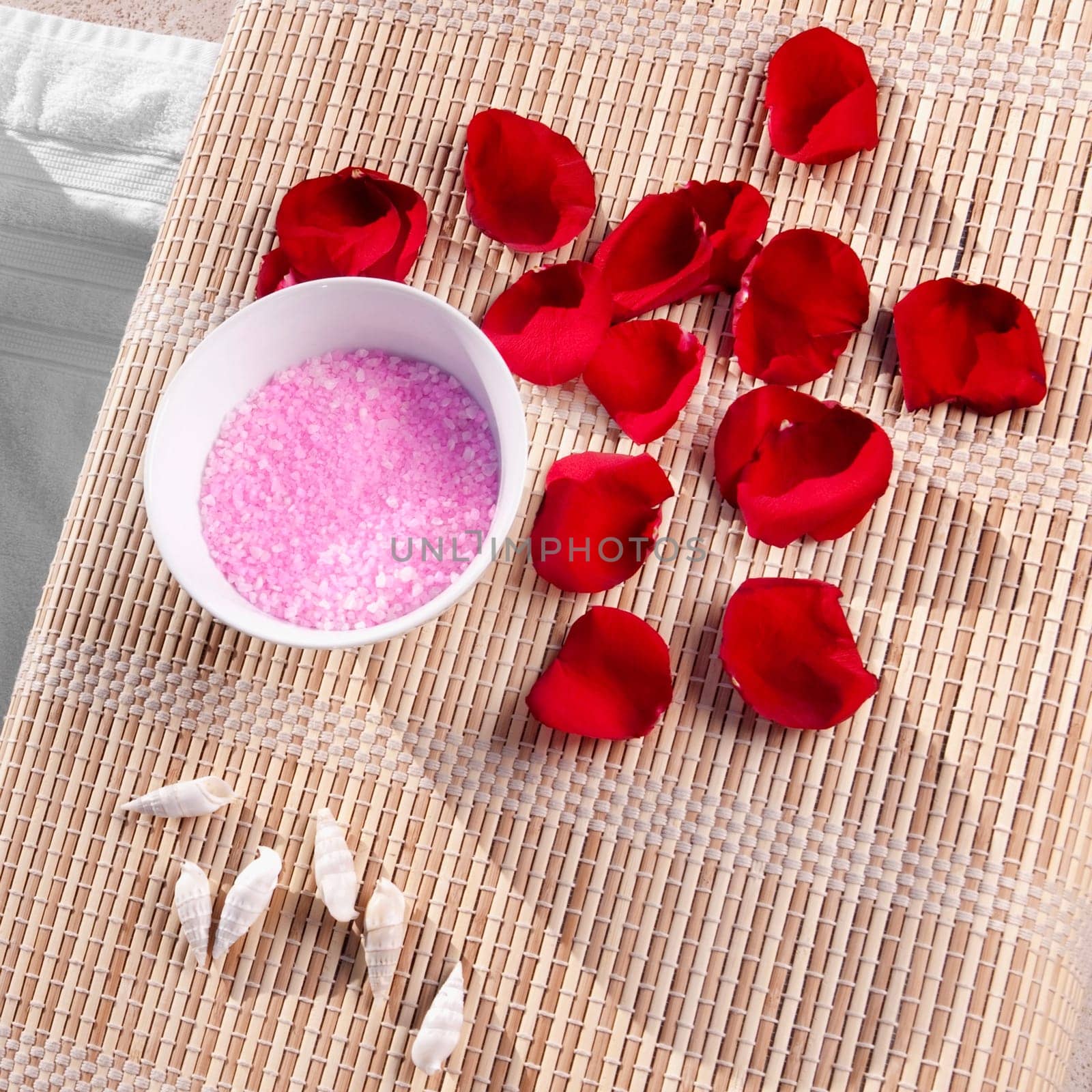 High angle view of bath salt and rose petals with shells on a bamboo mat