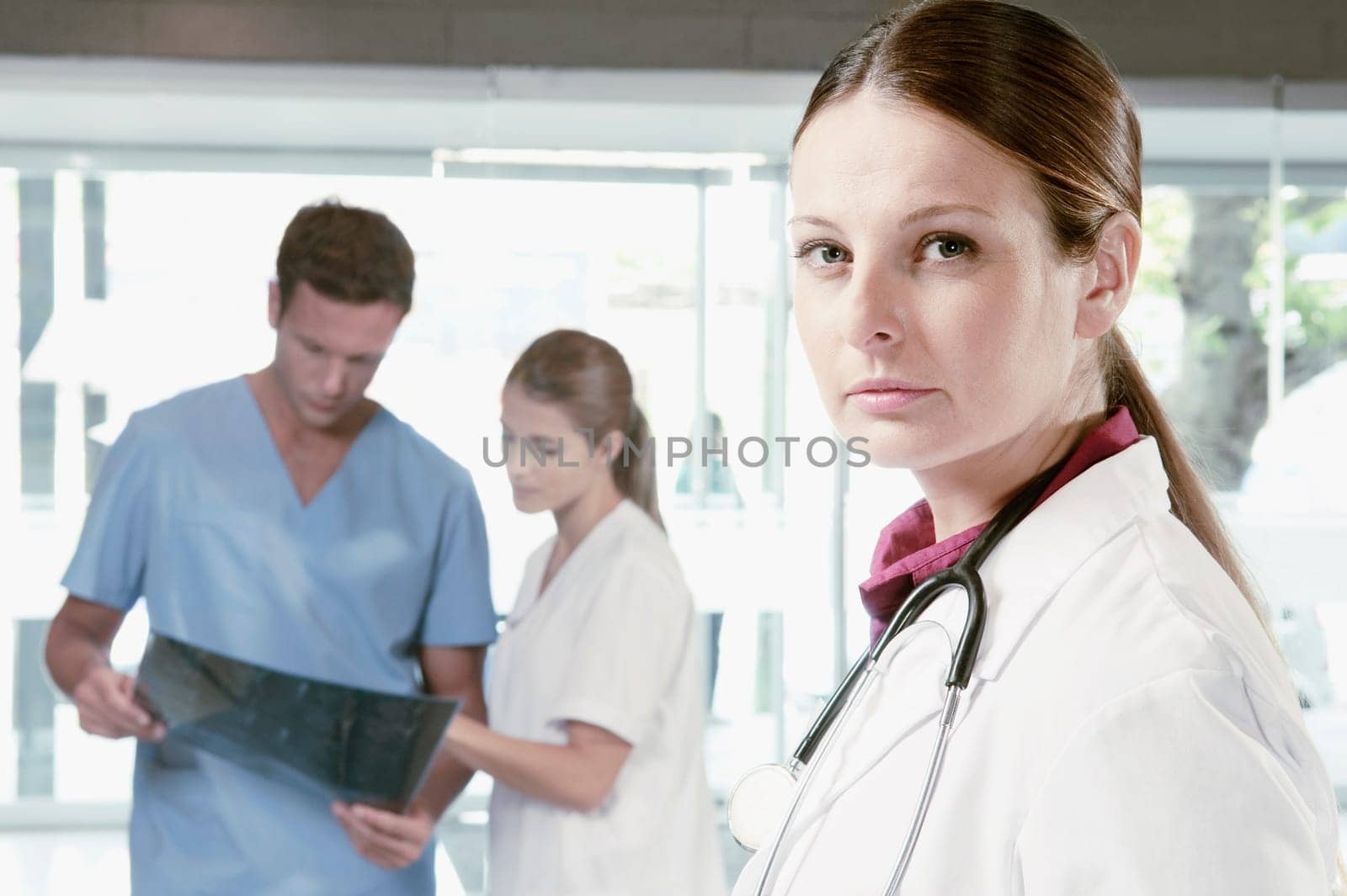 Portrait of a female doctor with her colleagues examining an X_Ray in the background