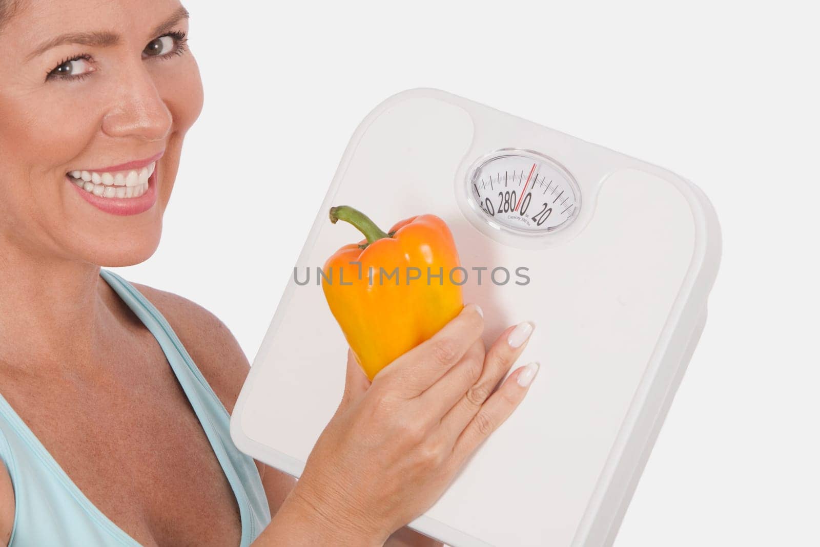 Woman holding a bathroom scale and an orange bell pepper and smiling