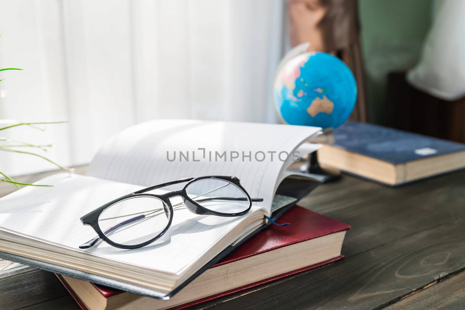 Reading glasses put on open books over wooden table beside the window