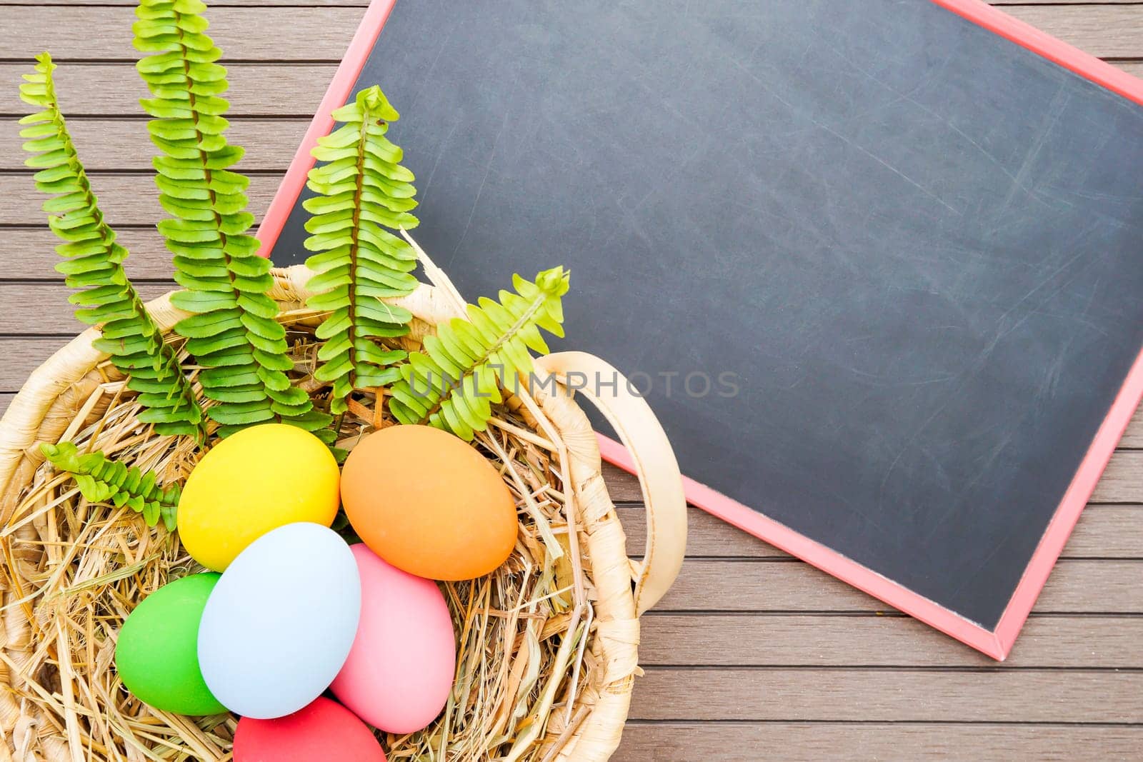Colorful easter eggs in the basket and blackboard on wood background with space