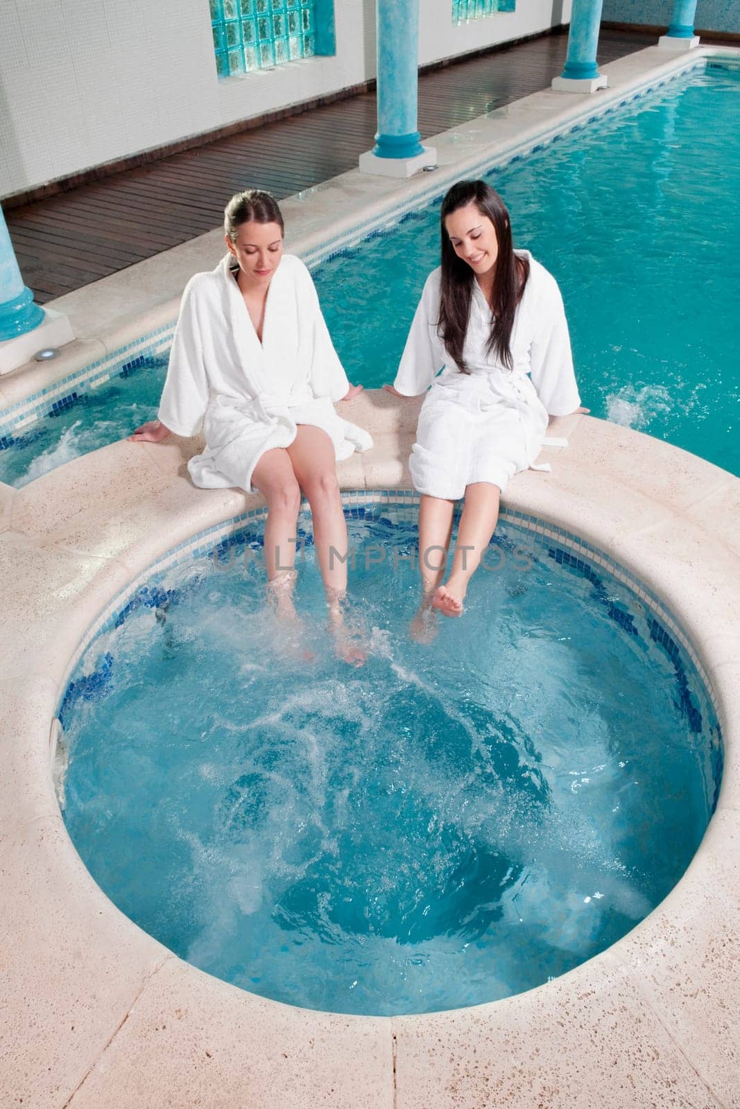 Two women sitting at the poolside with their feet soaking in water