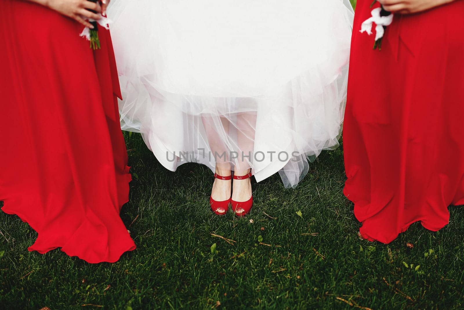 Bride in white dress with bridesmaids in red dresses on the green grass. Blurred background. High quality photo
