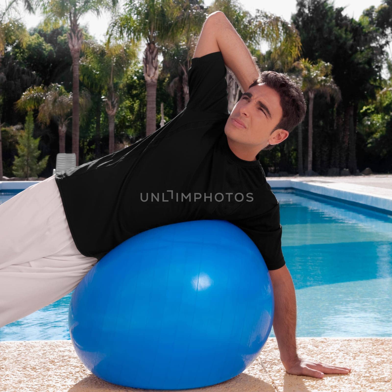Man exercising with a fitness ball at the poolside