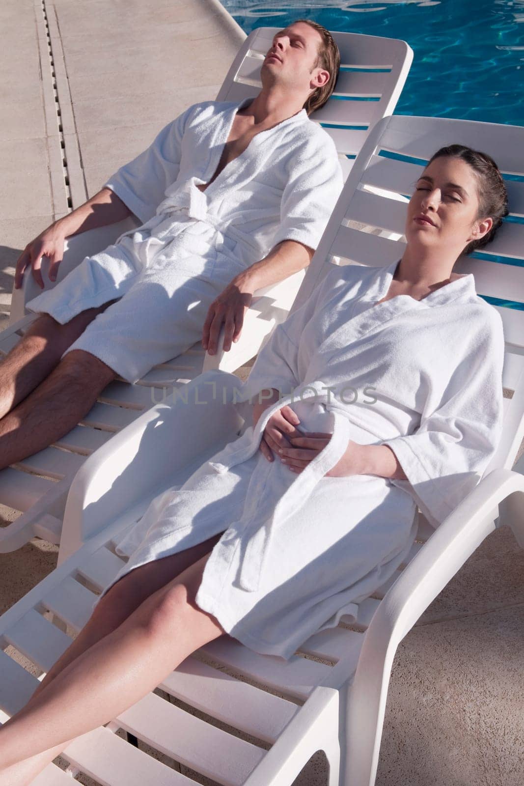 Couple resting on lounge chairs at the poolside