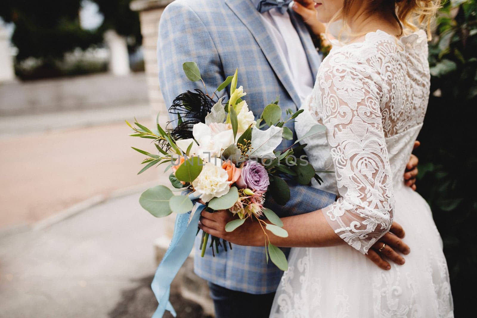 Bride in white dress is holding wedding bouquet. Groom hugs the bride. Blurred background. High quality photo
