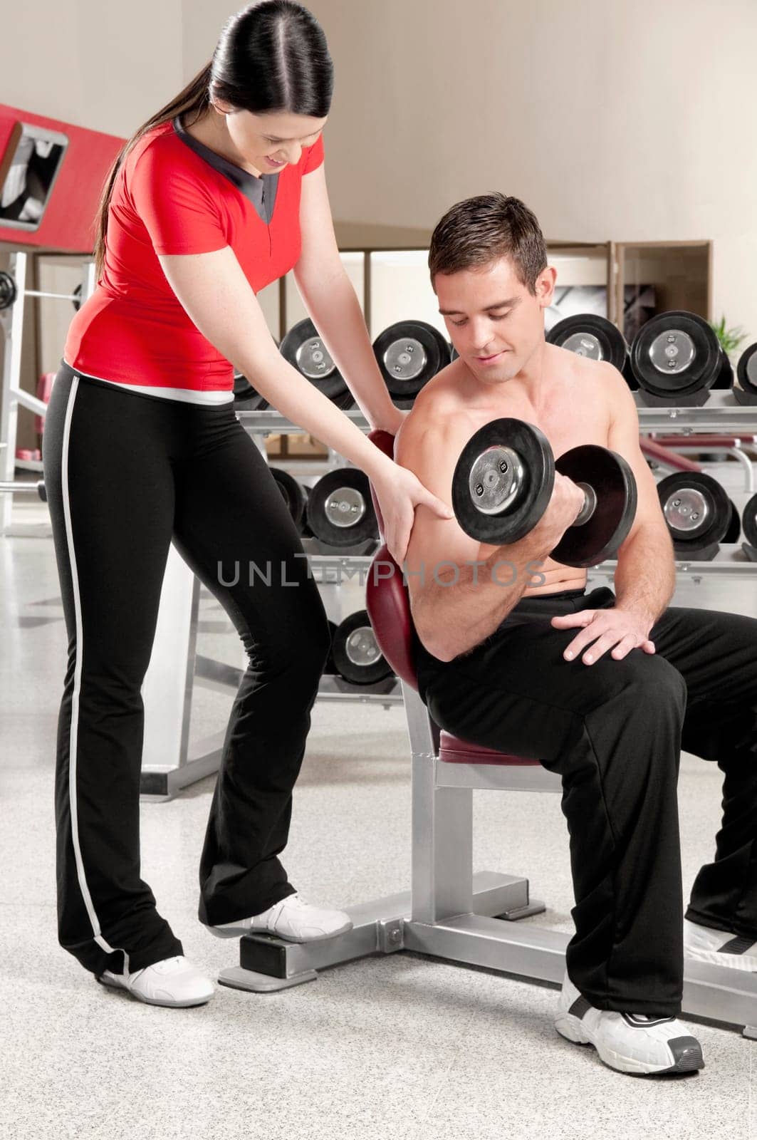 Woman touching a manŽs bicep as he exercising with a dumbbell