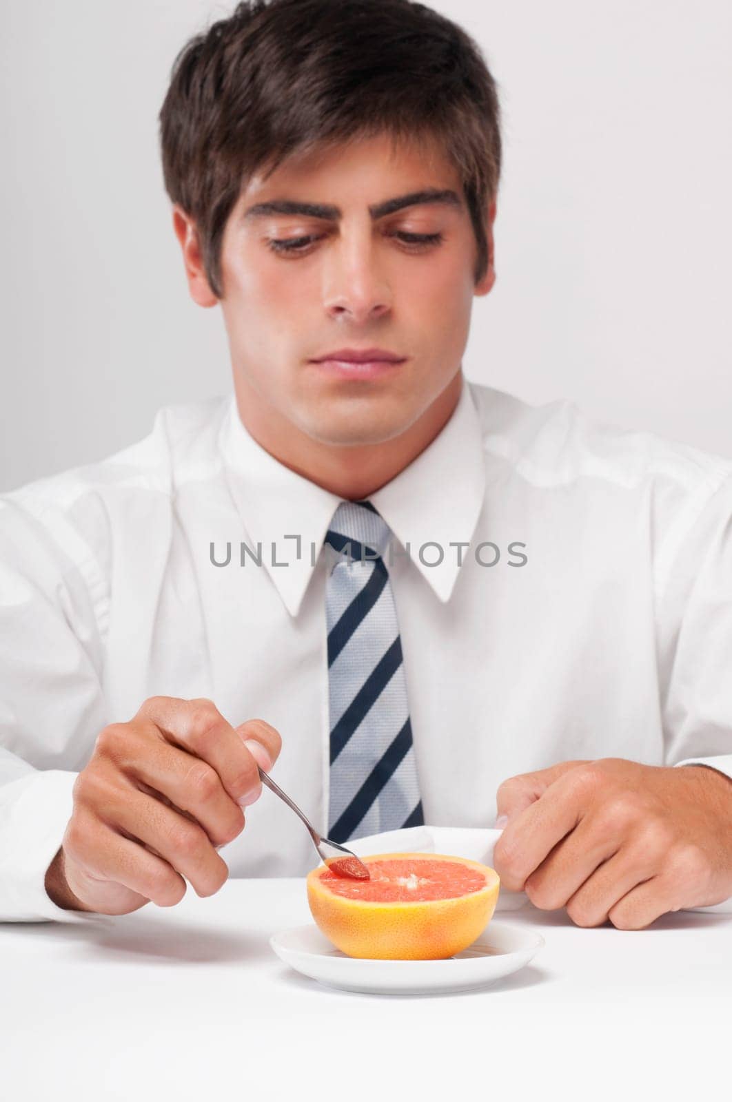 Close_up of a businessman eating a grapefruit with a spoon