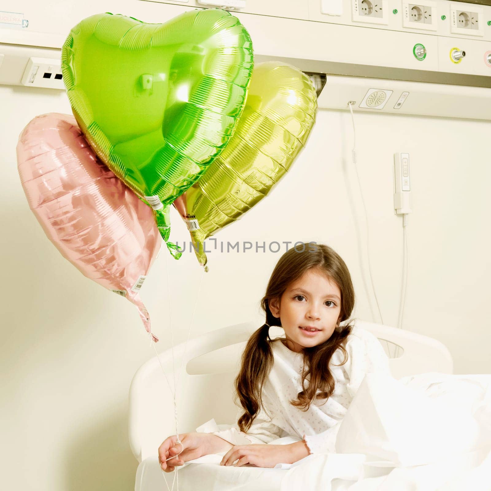 Girl with balloons on a hospital bed