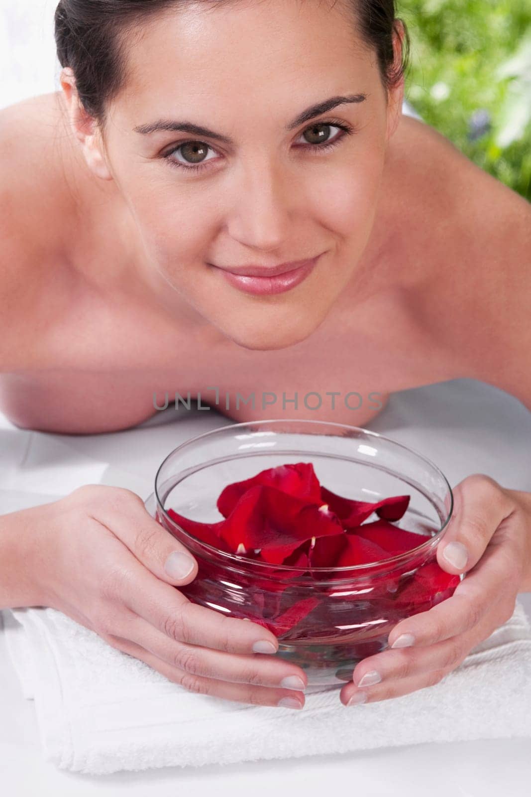 Portrait of a woman lying on a massage table holding a bowl of rose petals