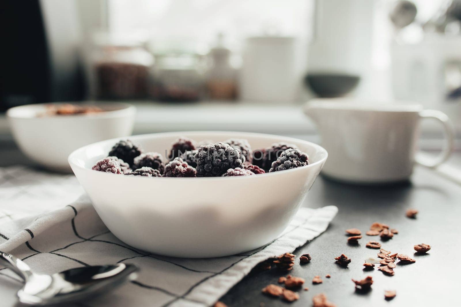 Frozen blackberries, granola, cream, towel on table. Blurred background. High quality photo