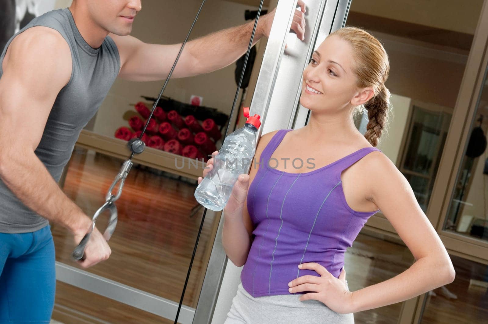 Man exercising in a gym with a woman smiling beside him