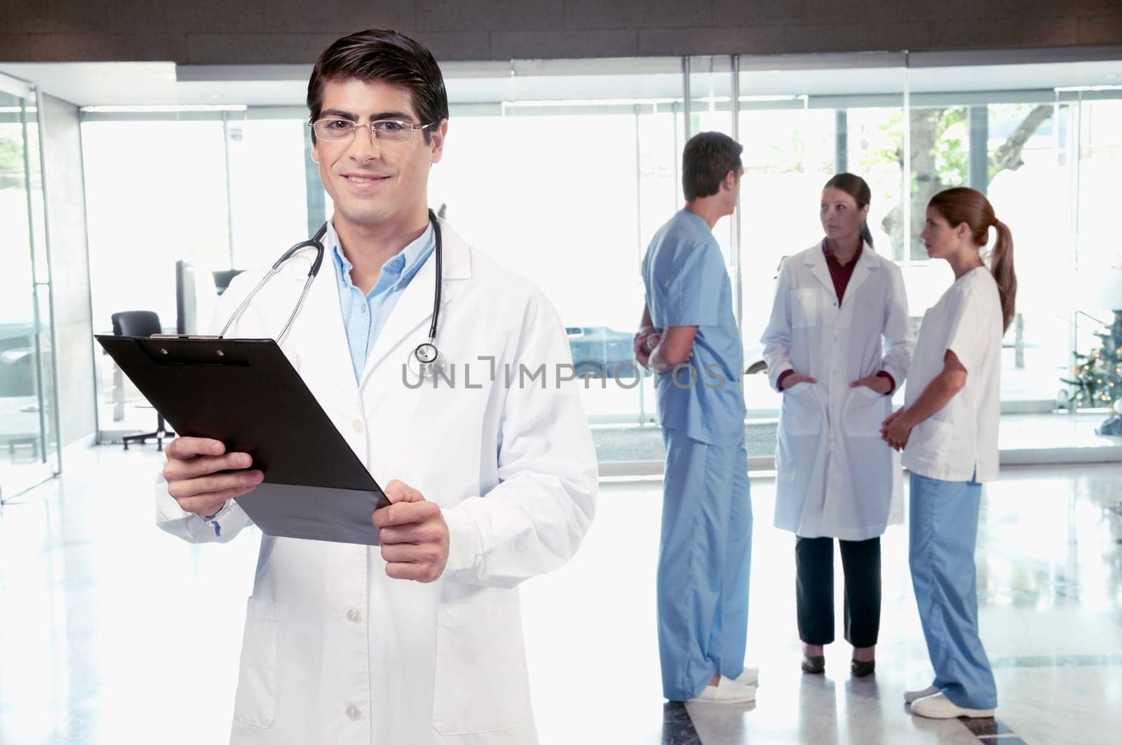 Doctor holding a clipboard with his colleagues discussing in the background