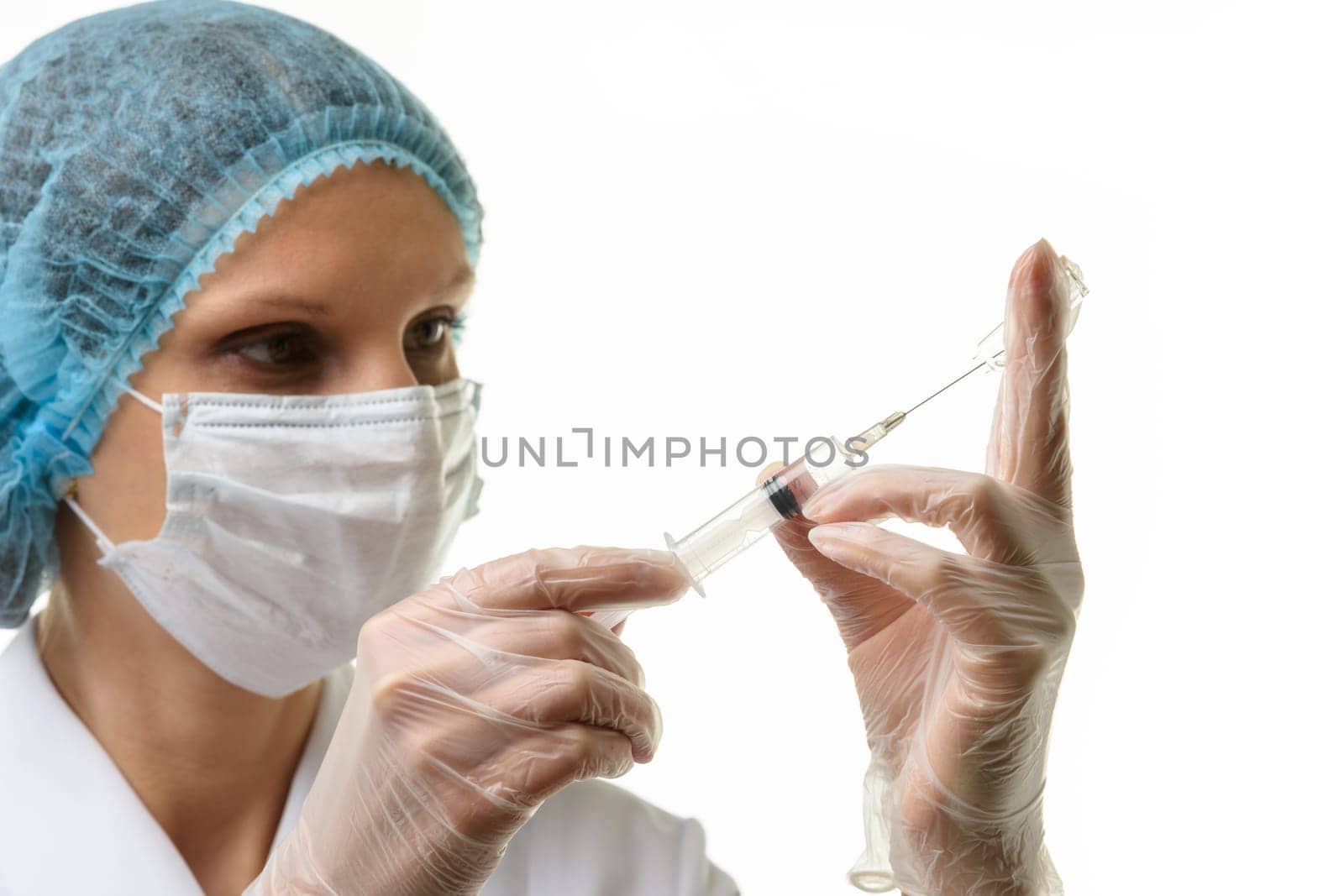 A nurse wearing a mask and gloves draws medicine with a syringe from an ampoule, isolated on a white background