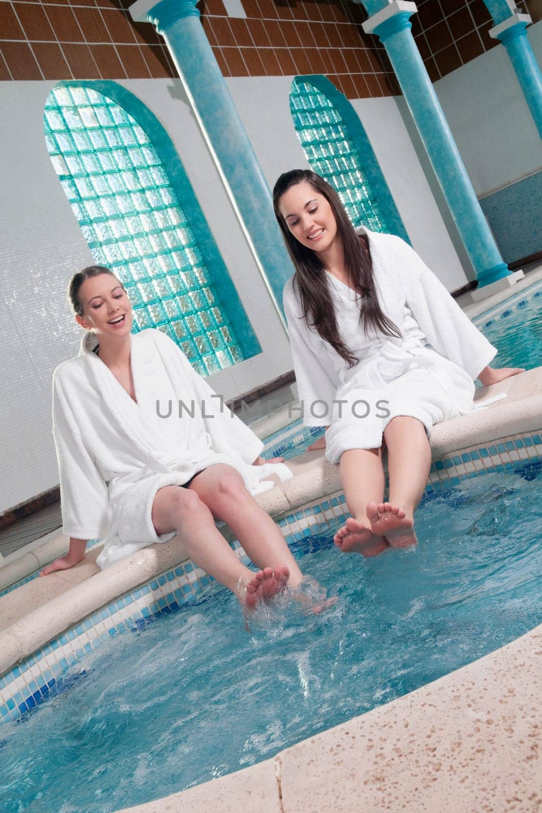 Two women sitting at the poolside with their feet soaking in water