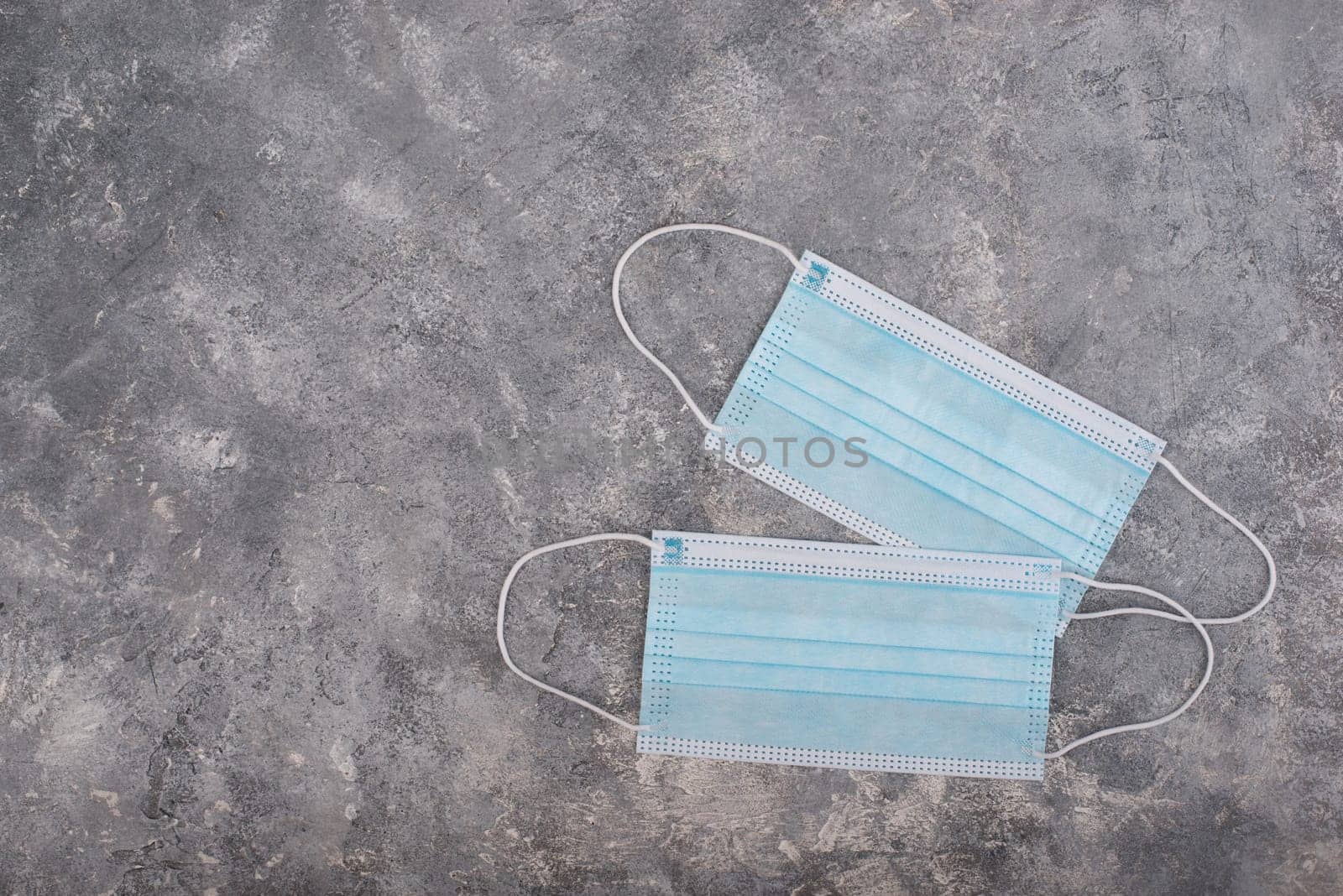 Surgeon masks to protect from Covid-19, worldwide pandemic in 2020 and 2021, blue coloured, empty copy space for text, isolated on a textured background