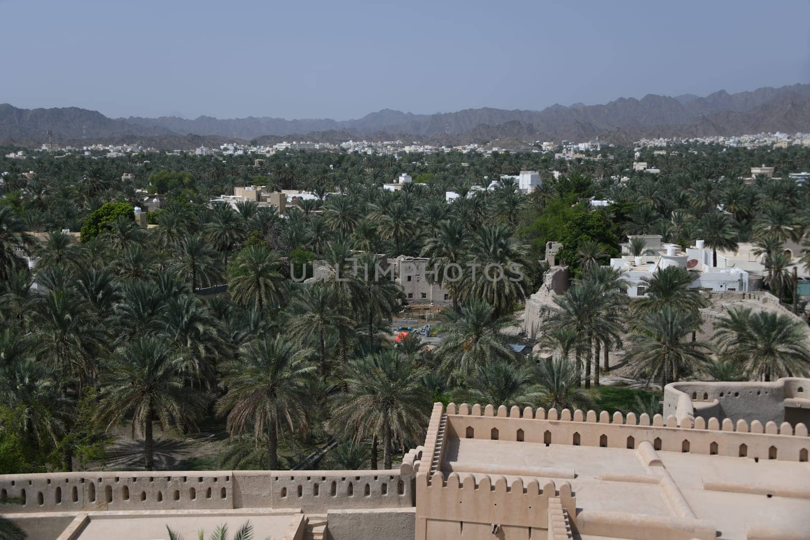 The oasis city of Nizwa is located at the foot of the Hajar Mountains and in the heart of Oman on the Arabian Peninsula. A panoramic view of the city's palm grove.