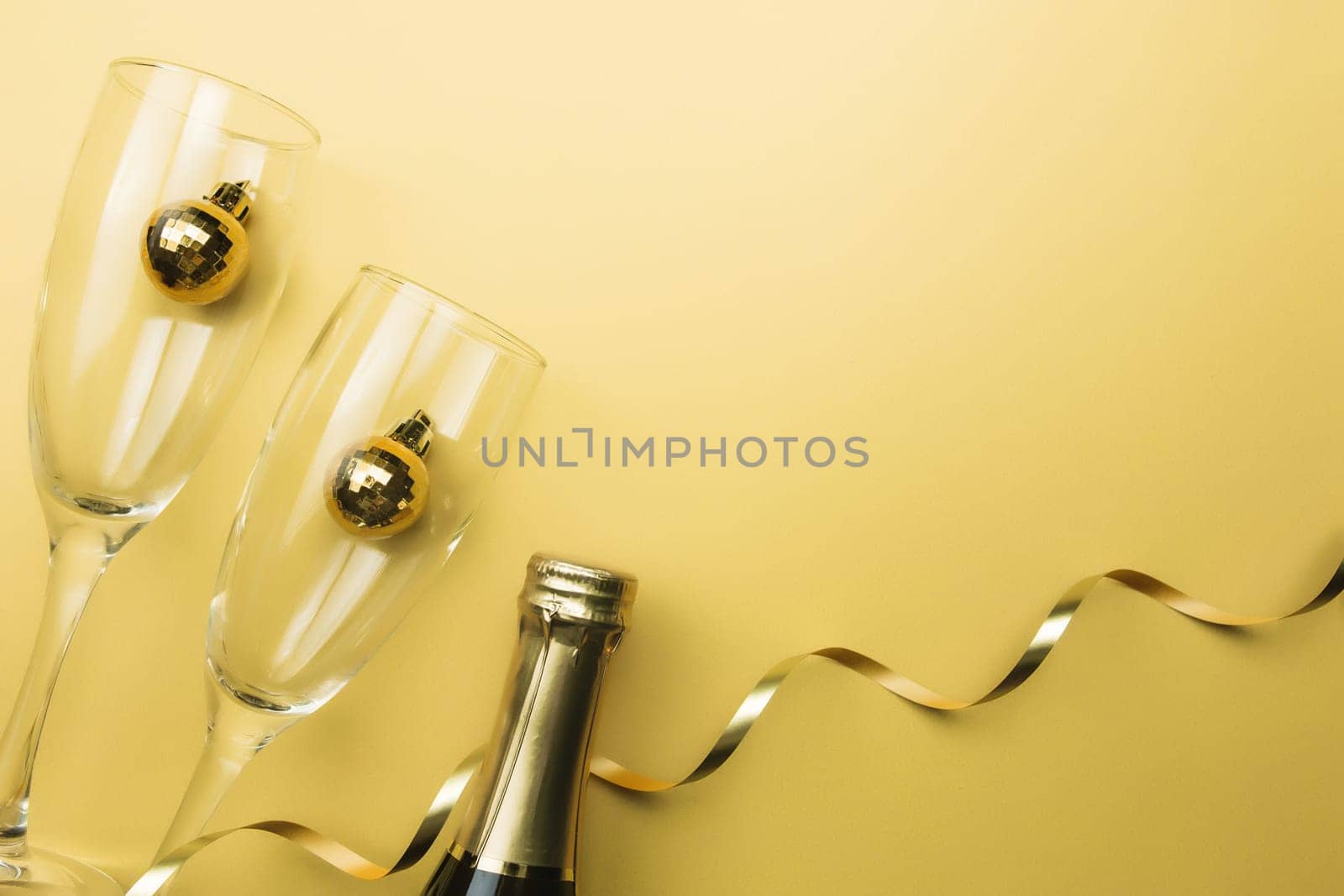 Glasses, sparkling wine bottle, christmas tree balls, ribbon, gold background. High quality photo