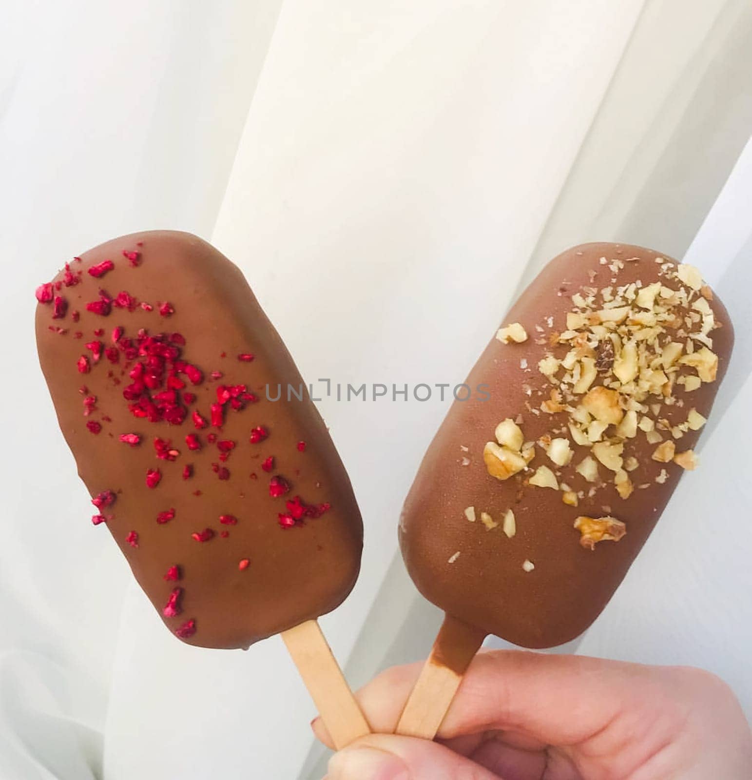 Two Eskimo ice creams on a wooden stick in hand.
