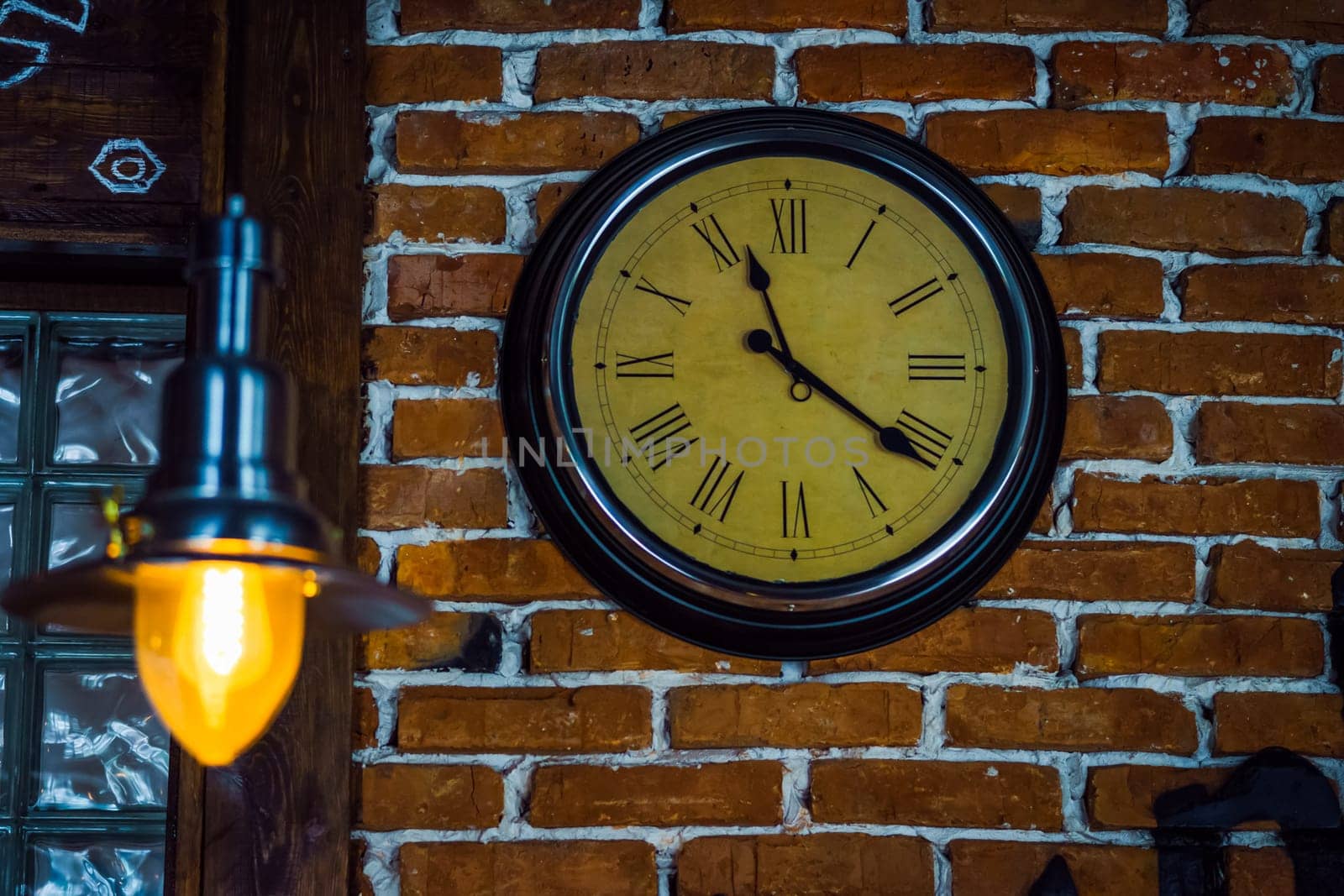 Round clock with Roman numerals hang on a brick wall