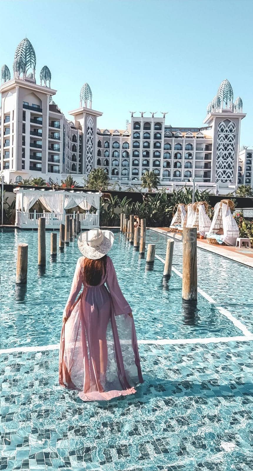 A girl walks around the pool in a dress. small pool near the hotel.