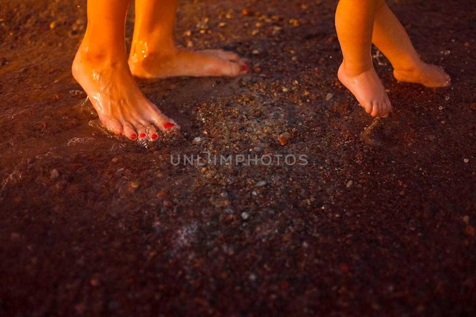 The legs of the baby and mother on the beach. Swimming in the sea with a child.