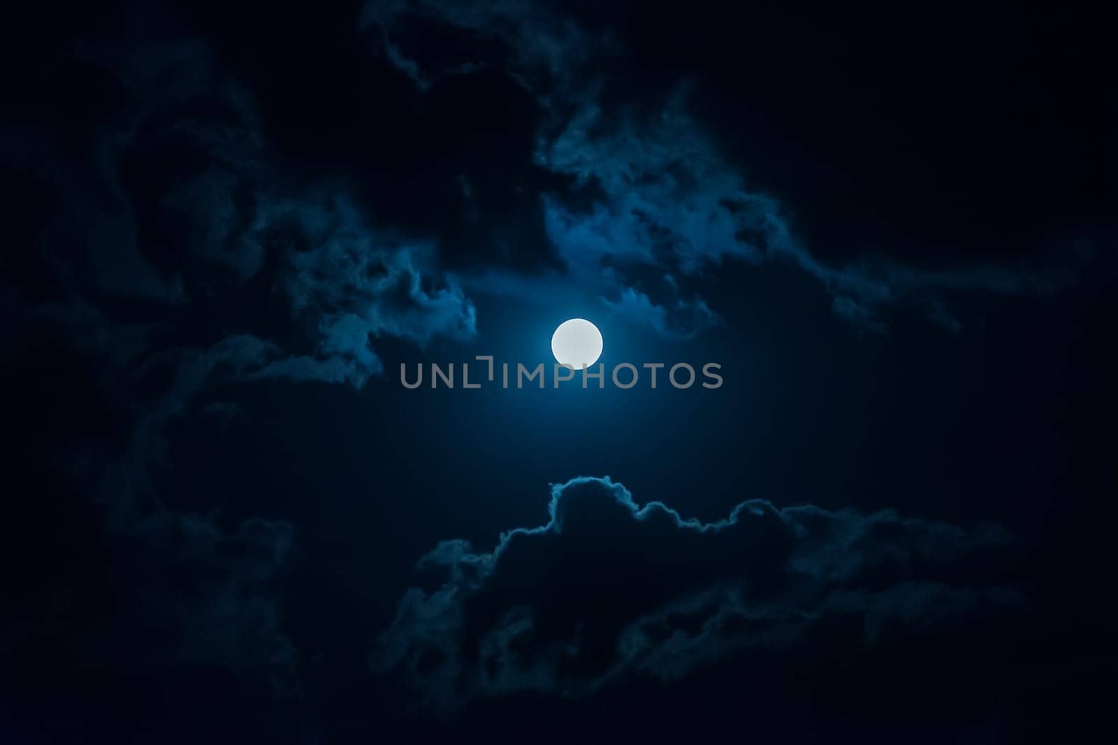 A full moon in the night sky among the clouds.