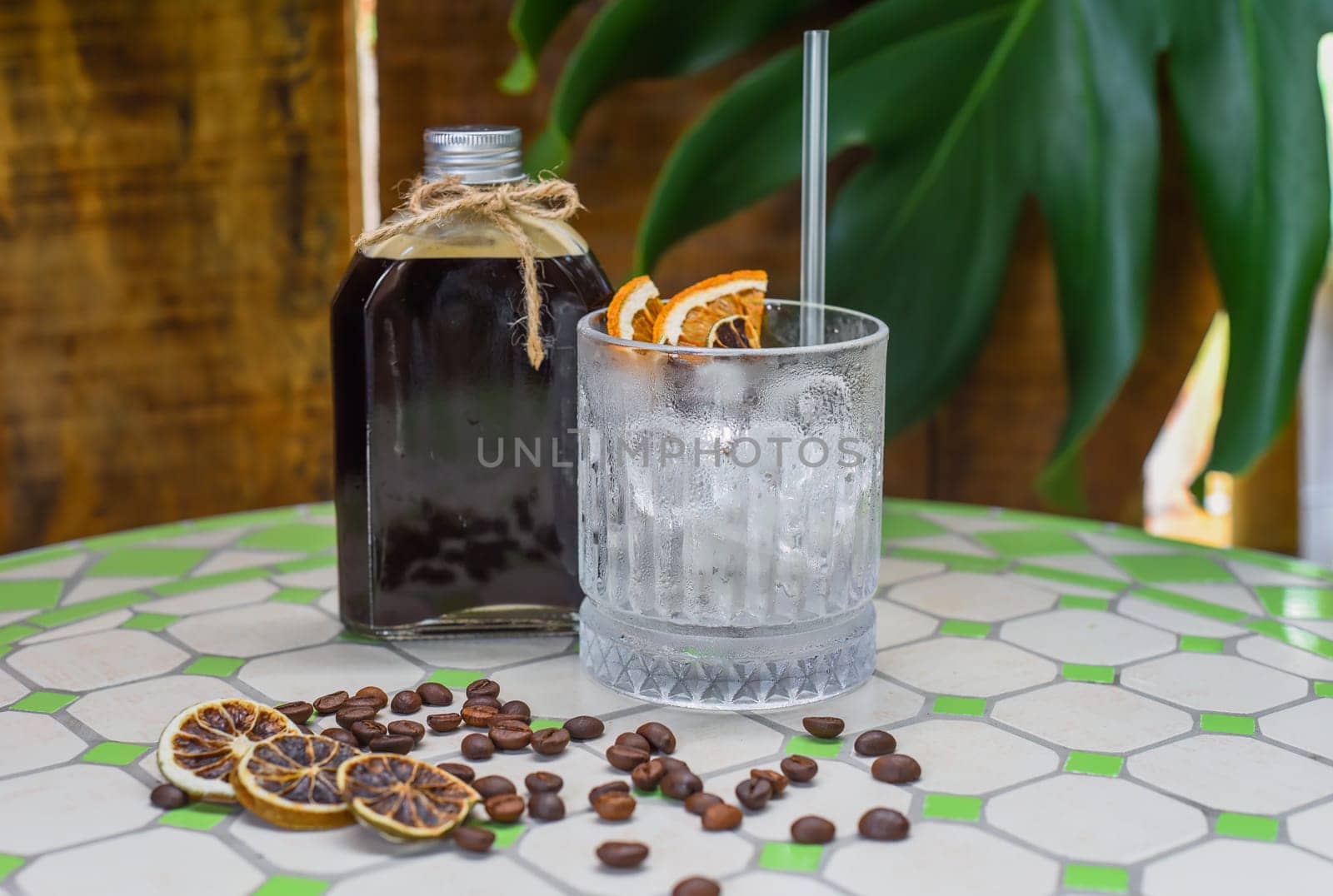 Cold brew coffee in a bottle with transparent glass full of ice on green leaves background