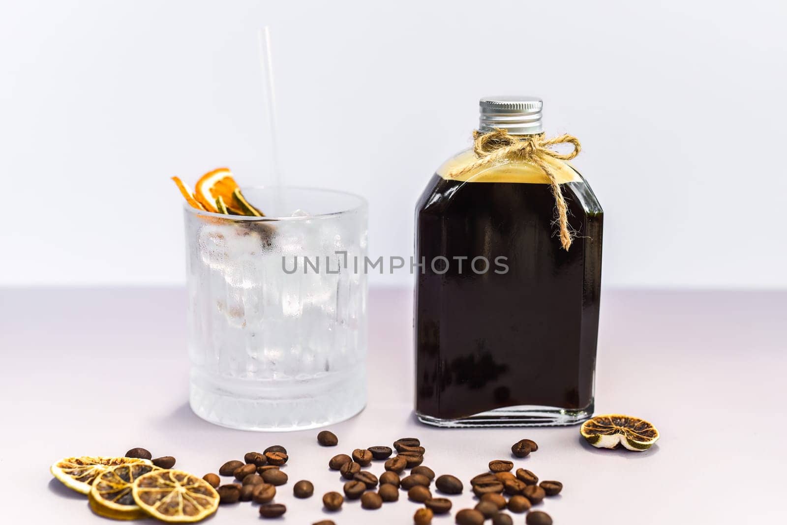 Cold brew coffee in a bottle with transparent glass full of ice on light gray background