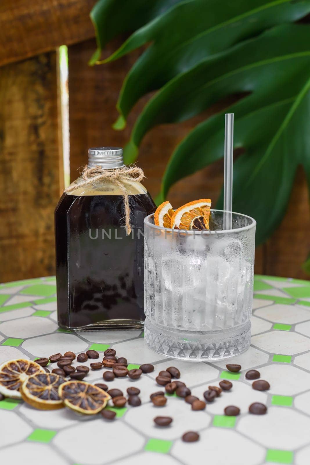 Cold brew coffee in a bottle with transparent glass full of ice on green leaves background
