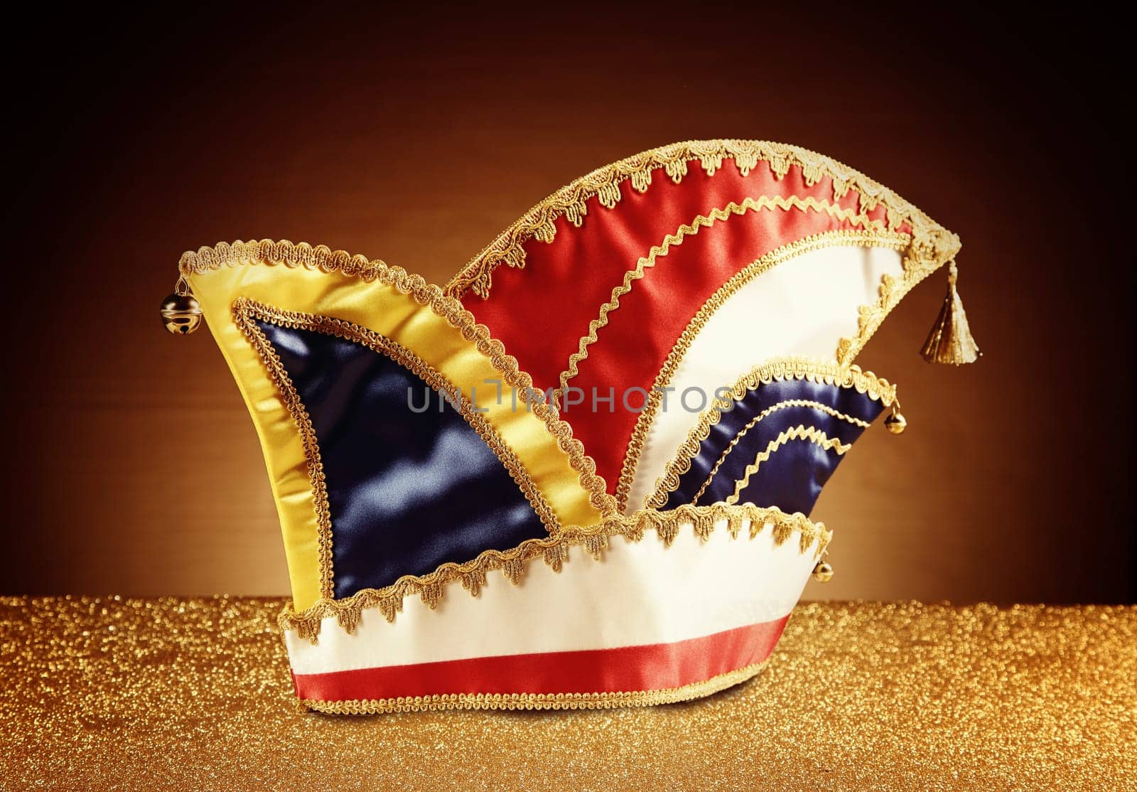 Close up Attractive Carnival Jester Hat on Glittery Platform in Front Gradient Brown Background.
