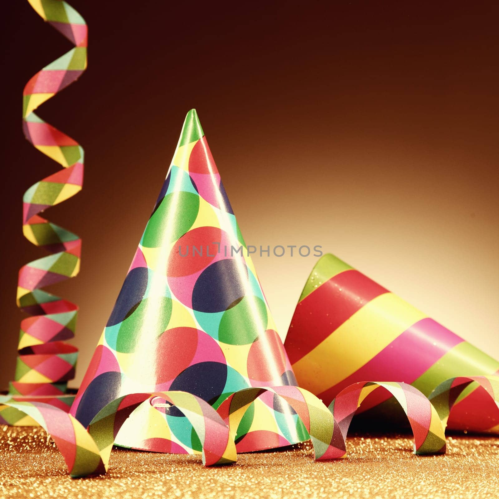 Close up Carnival Hats and Paper Streamers on Platform with Golden Particles in front Gradient Brown Background.