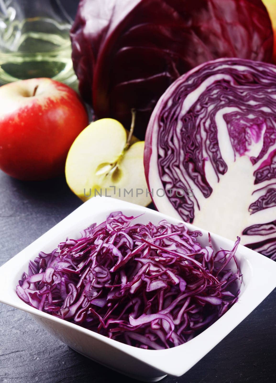 Close up Shredded Purple Cabbage on White Bowl on Top of the Table with Apples and Other Cabbage.