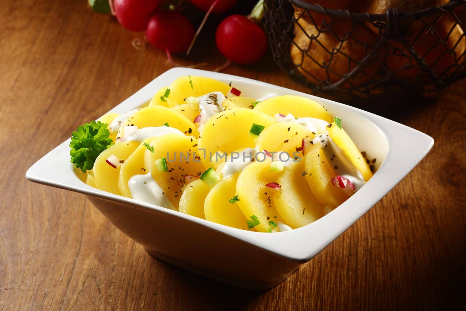 Close up Appetizing Flavored Boiled Potato salad with White Cream and Spices on White Bowl. Placed on Wooden Table.