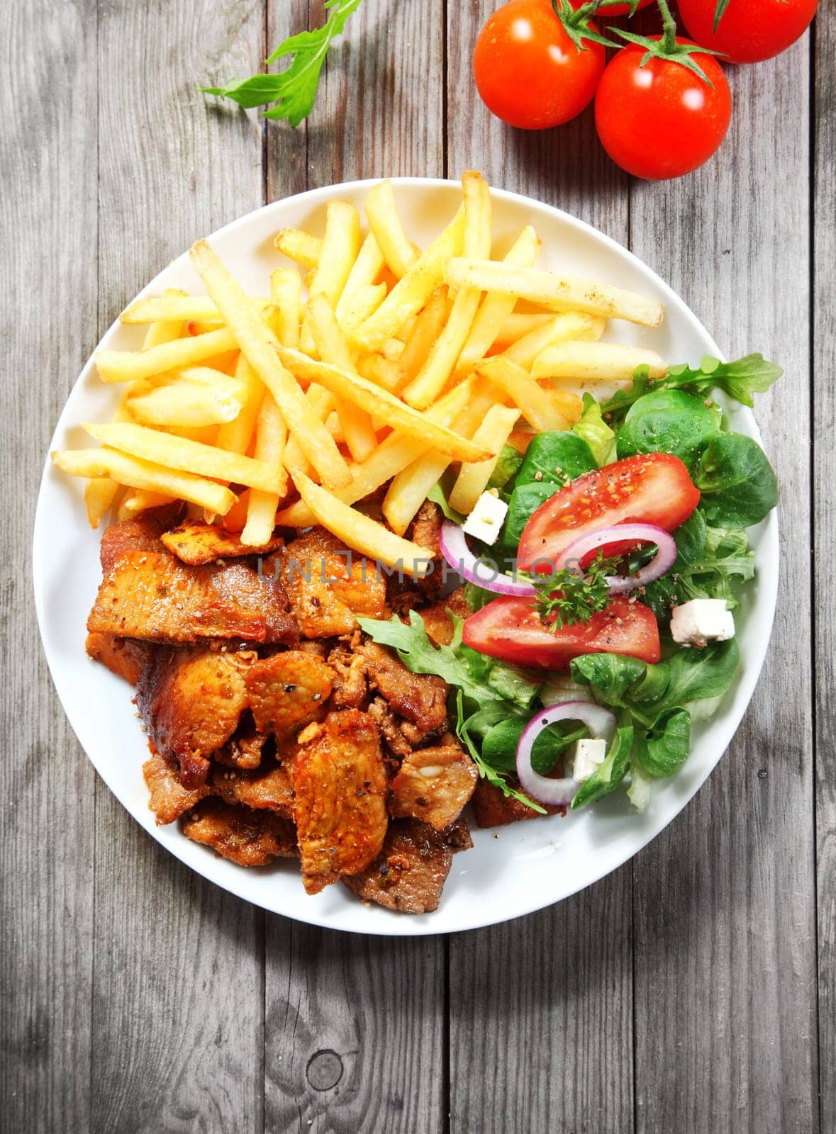 Close up Tasty Main Dish with Beef Steak, Fried Fries and Fresh Veggies on White Plate, Served on Wooden Table.
