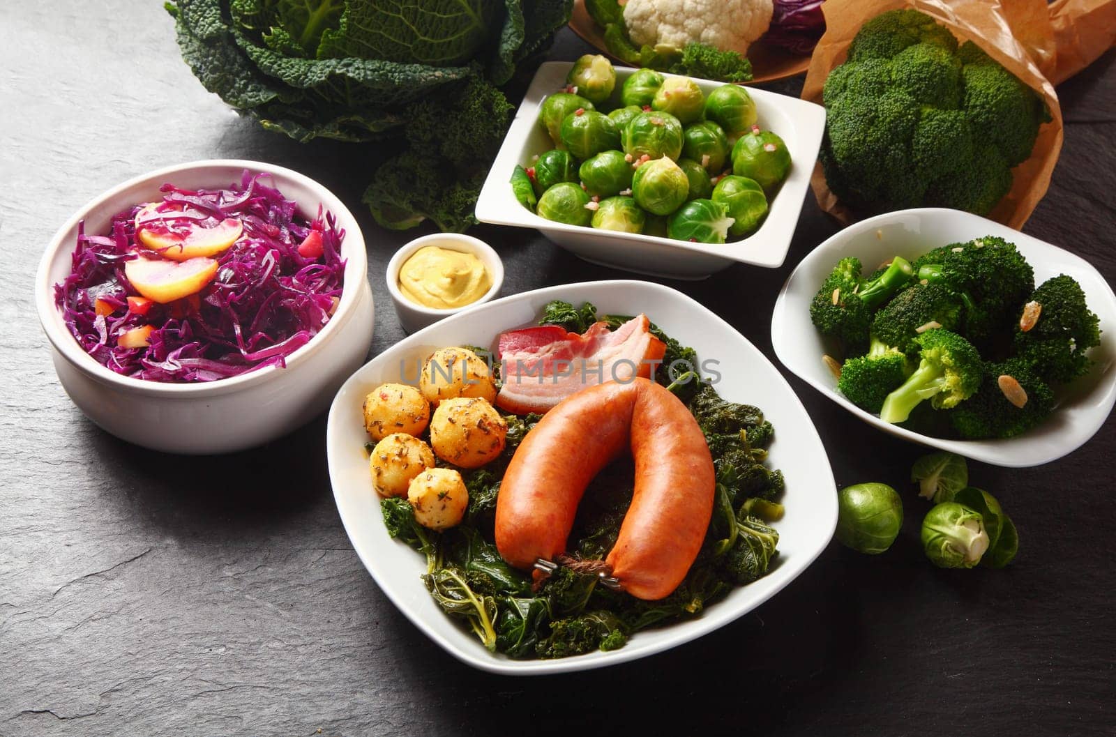 Close up Gourmet German Recipe with Sausage, Meat and Potatoes on Top of Green Veggies Placed on Wooden Table with Fresh Veggies on Sides