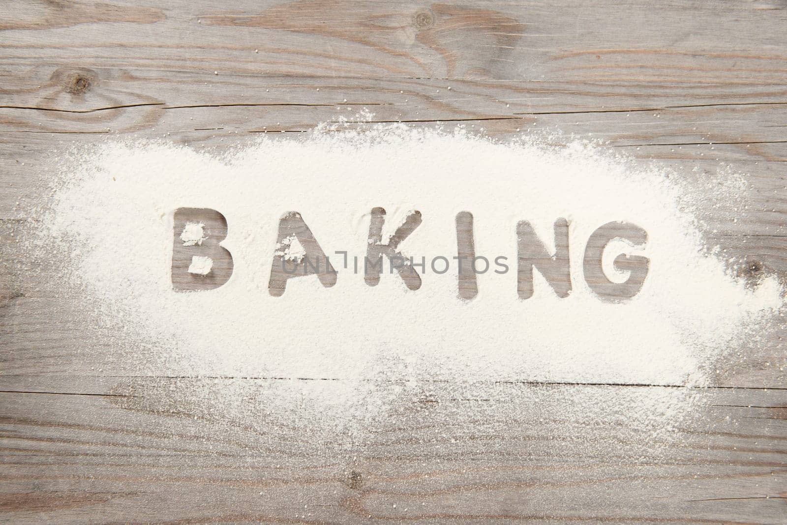 Word baking written in white flour on a old wooden table, low light vintage tone.