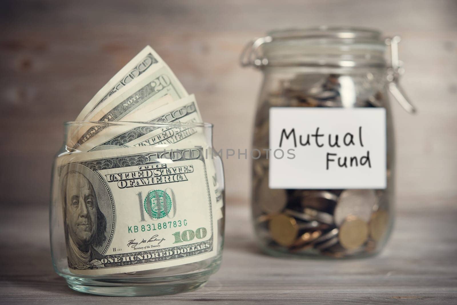 Dollars and coins in glass jar with mutual fund label, financial concept. Vintage tone wooden background with dramatic light.