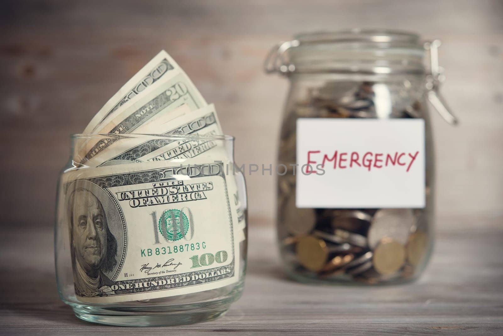 Dollars and coins in glass jar with emergency label, financial concept. Vintage tone wooden background with dramatic light.