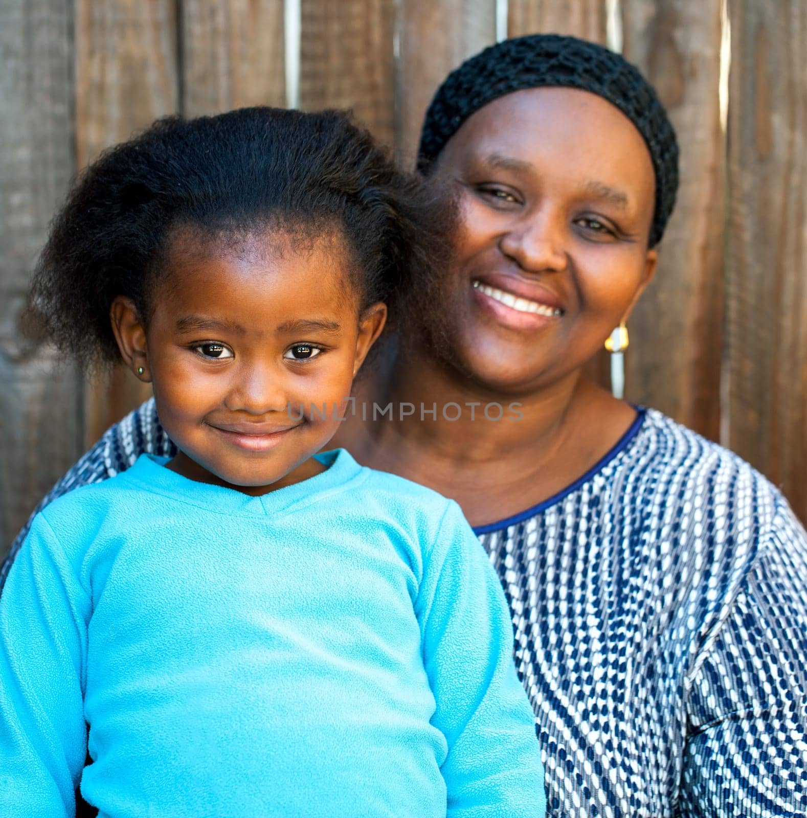 Portrait of african mom and daughter against wooden fence.