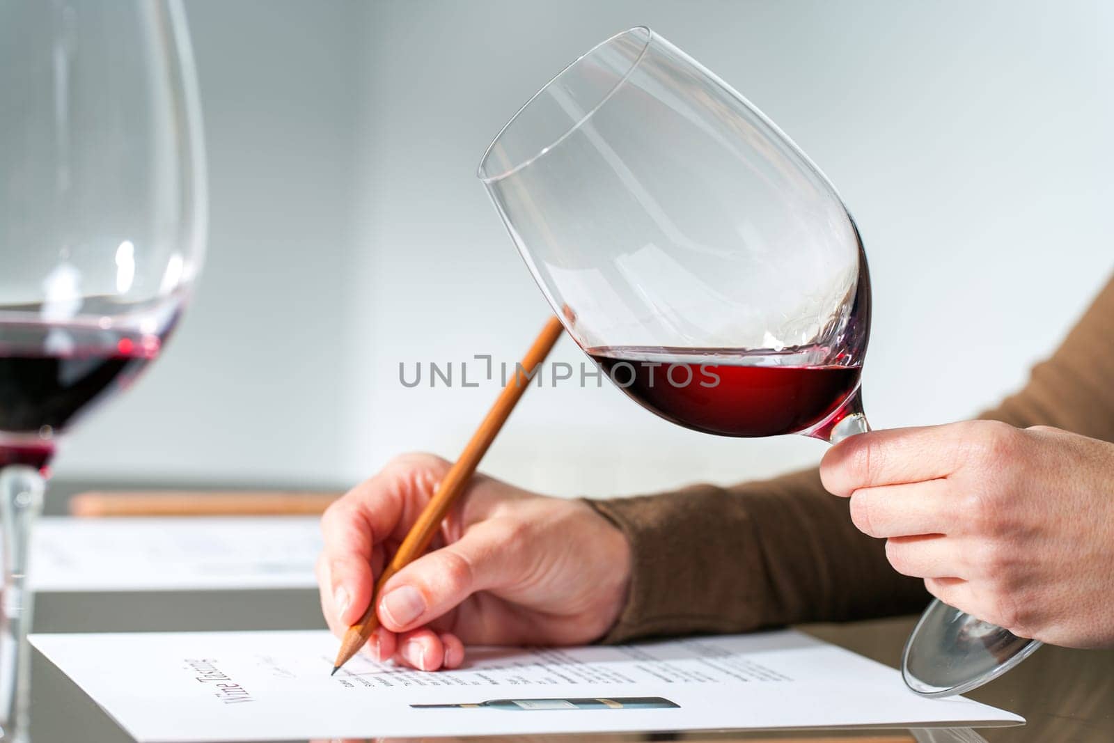 Extreme close up of sommelier evaluating red wine in wine glass at tasting..
