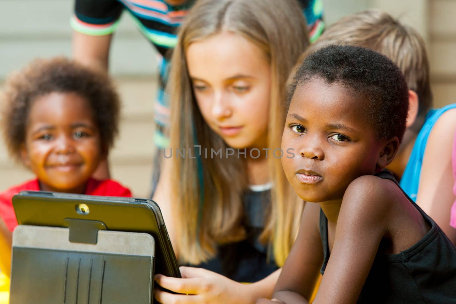 Portrait of small African girl with group of friends outdoors.